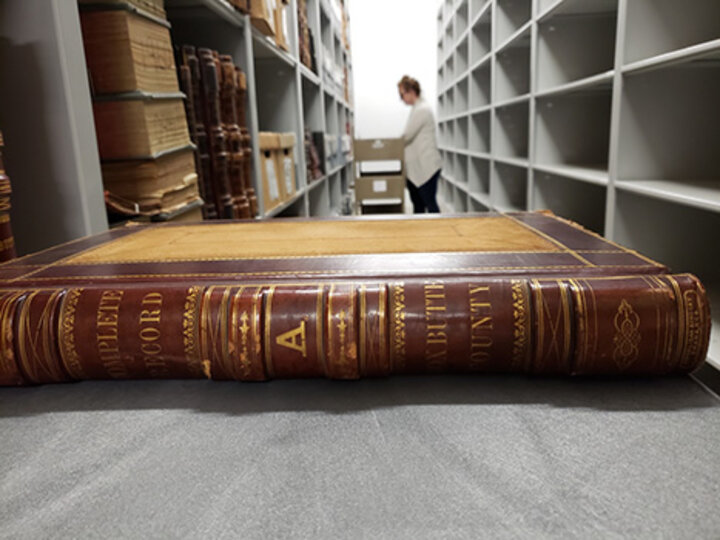 This photo shows a closeup of a book in the foreground. A woman stands in the distance with a cart of books.