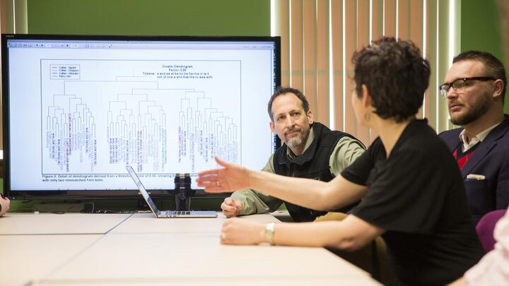 Photo of project team sitting at a desk looking at a chart on a large computer screen.