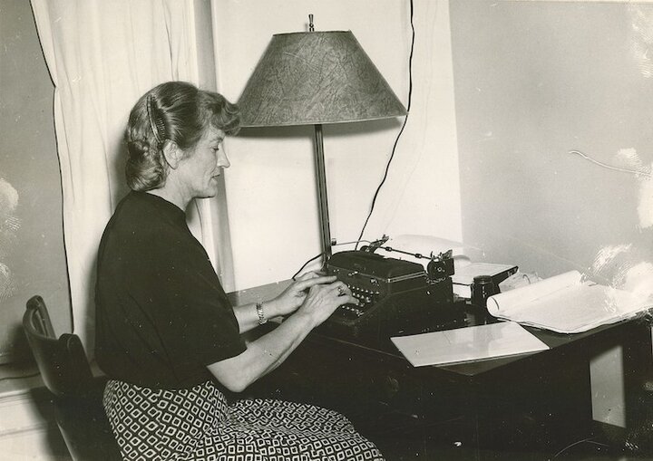 Black and white photo of Mari Sandoz. She sits at a table with a typewriter.