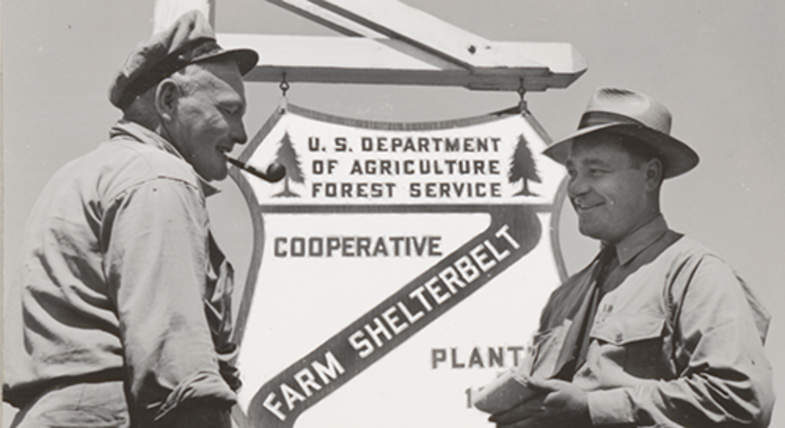 Two men standing in front of a U.S. Department of Agriculture Forest Service sign. 